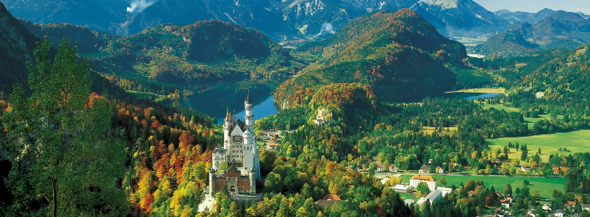 Panoramablick auf das Schloss Neuschwanstein im Allgäu und die umliegende Bergkulisse.